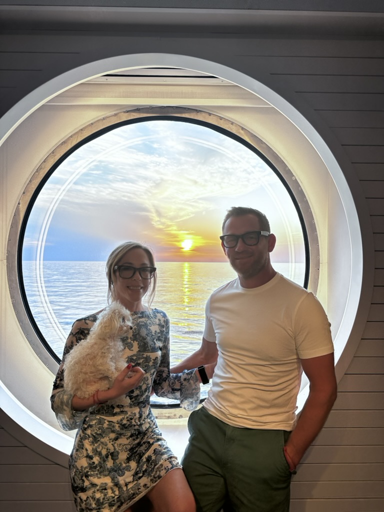 Tim and Nicci Grotefendt, owners of GHR Egress Windows, standing in front of a round ship window on a Mediterranean cruise.