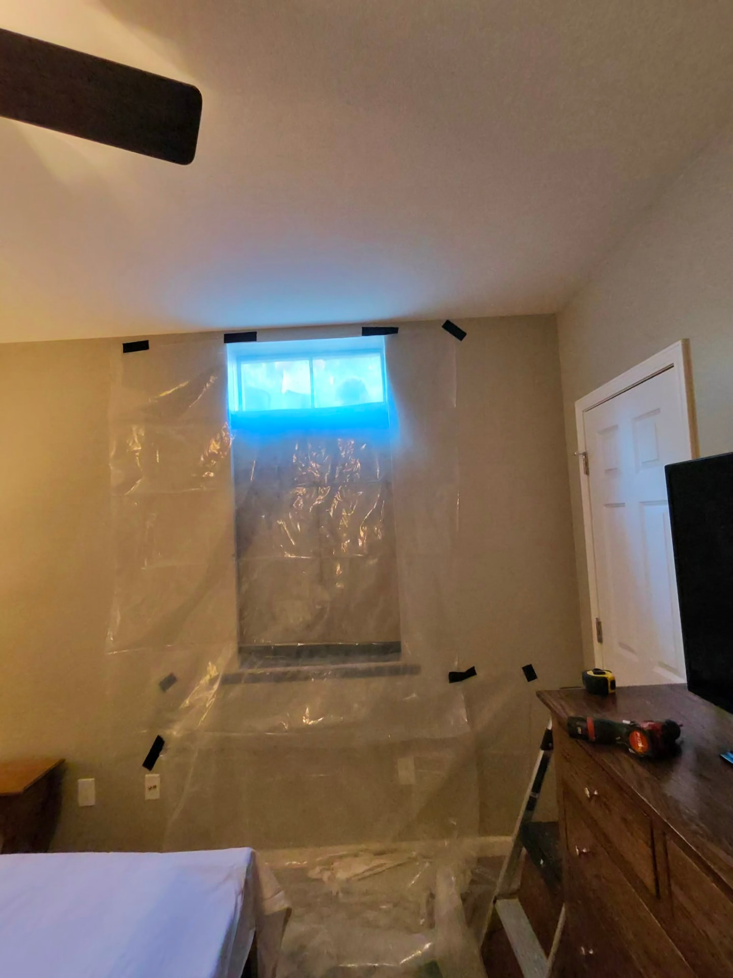 Plastic sheeting set up around a basement window opening during egress window installation, furniture left in place, Godfrey, Illinois, GHR Egress Windows.