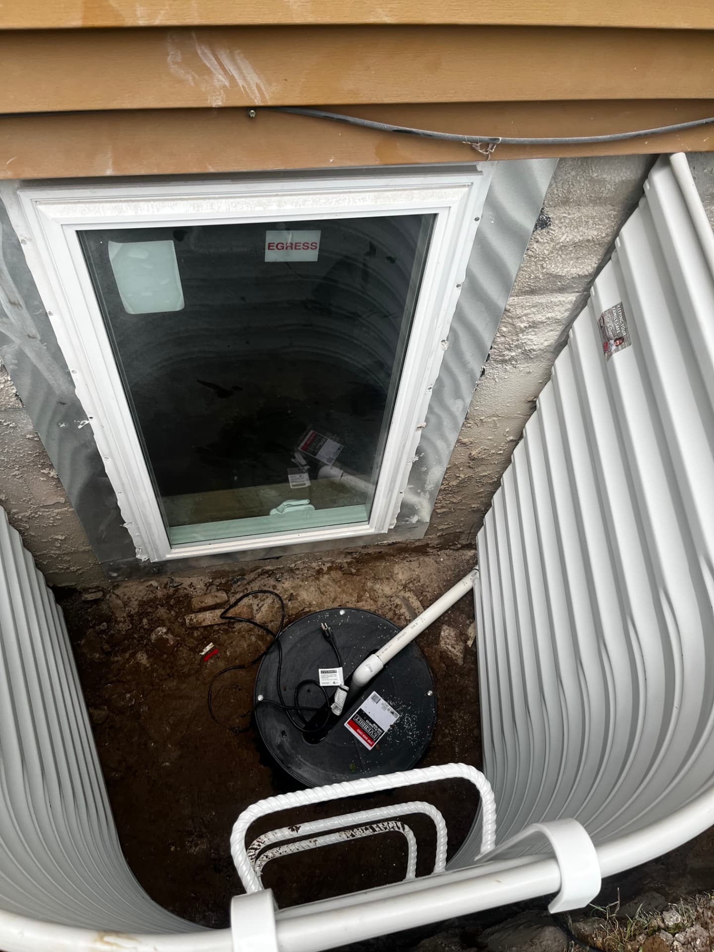 Sump pit with pump and discharge line set at the bottom of an egress window well, installed by GHR Egress Windows.
